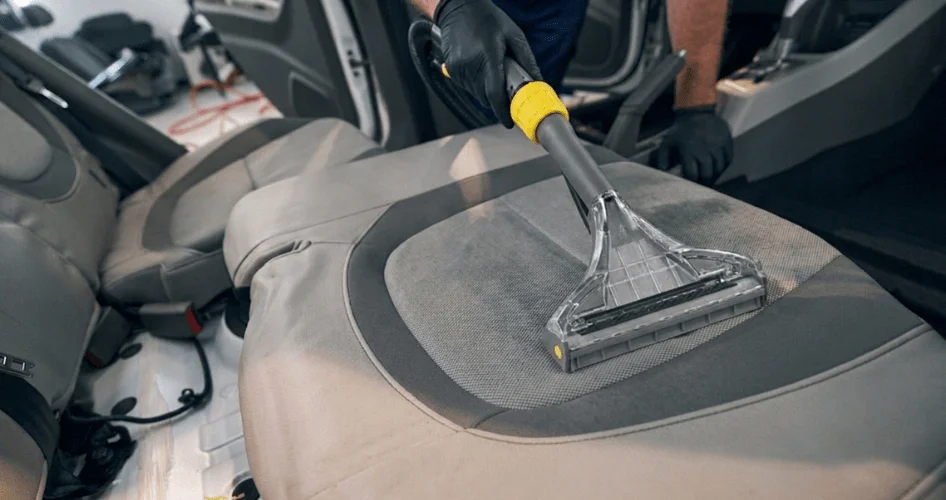 Professional car interior cleaning using a handheld upholstery tool on a fabric seat.