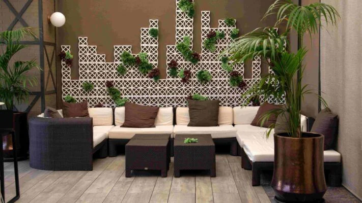 Outdoor lounge with cream sofas, brown cushions, black wicker coffee tables, and a lattice wall with green plants in a patio setting