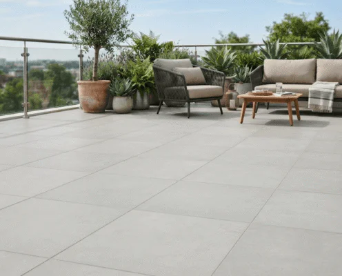Modern rooftop terrace with large grey tiled floor, potted plants, and beige outdoor seating around a wooden coffee table.