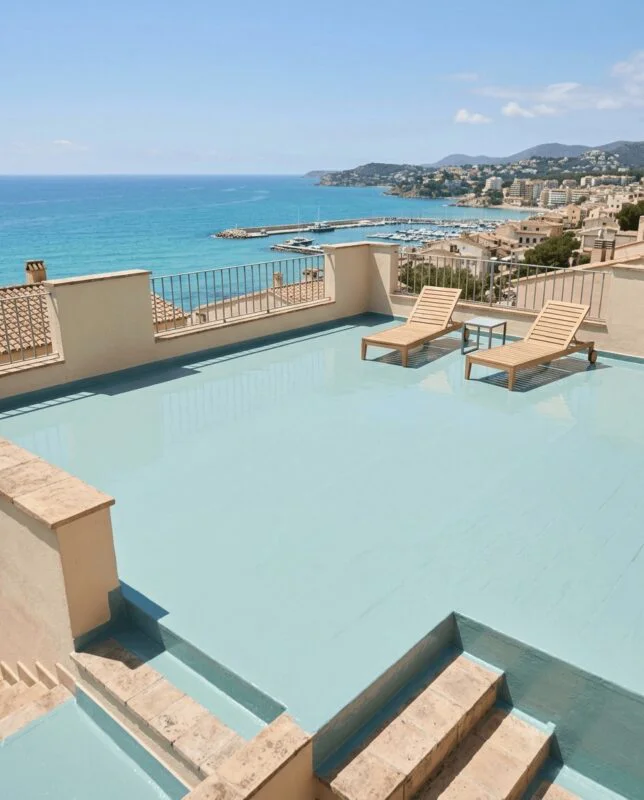 Rooftop terrace with a light blue pool and two wooden lounge chairs overlooking the sea and harbor.